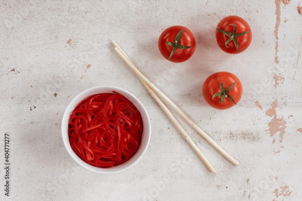 Fototapeta the texture on the surface of the red noodles in a bowl, ripe tomatoes and chopsticks