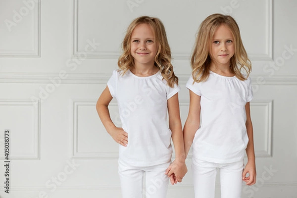 Obraz Two little kids girls in white clothes isolated on white background. Childhood concept. Twin girls they hold hands.