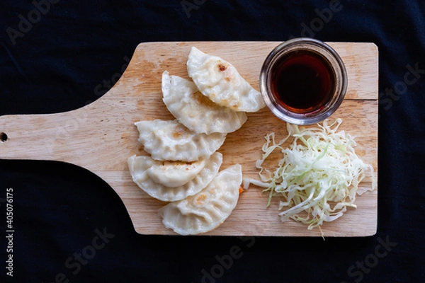 Obraz Japanese grilled gyoza dumplings with soy sauce on a wooden plate.