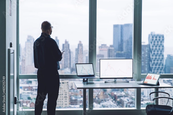 Fototapeta Unrecognizable businessman with smartphone near multimedia gadgets with graphs