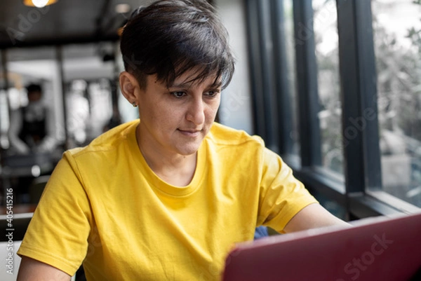 Obraz Young woman in trendy yellow colored t-shirt working on computer. Colors of the year 2021.