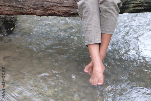 Fototapeta Legs of a woman in pants who sitting on a wood bridge and swinging her feet in a river