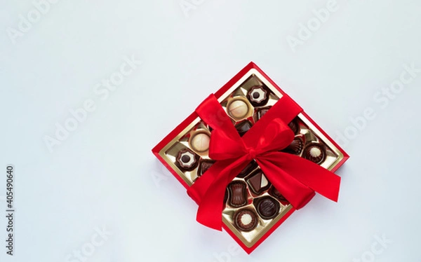 Fototapeta Box of chocolate pralines with red bow on light blue background. Image with copy space