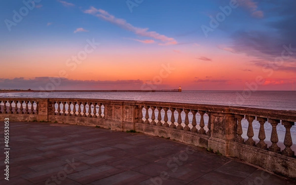 Fototapeta Beautiful colorful sunset over the Blyth Beach and the lighthouse in the background. View from the promenade. Pink blue sky with clouds.