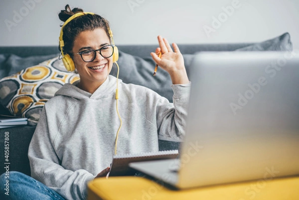 Fototapeta Millennial woman having video call on her computer at home. Smiling girl studying online with teacher.