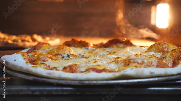 Obraz Male cook taking out four cheese pizza from electric oven using a shovel and putting it table at cuisine. Young cook baked delicious dish at kitchen restaurant. Concept of preparing food. Slow motion