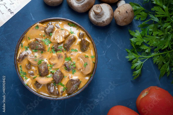 Obraz Traditional beef stroganoff with cream of champignon mushrooms in a blue bowl with its ingredients seen from above