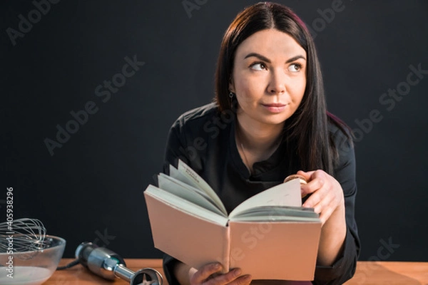 Fototapeta Excited female is going to cook something special, reading cookbook.