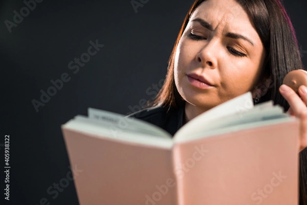 Fototapeta Young woman reading book while tasting a macaroon.