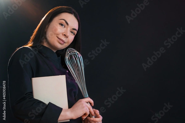 Fototapeta Exited female is going to cook, holding a cookbook and eggbeater.