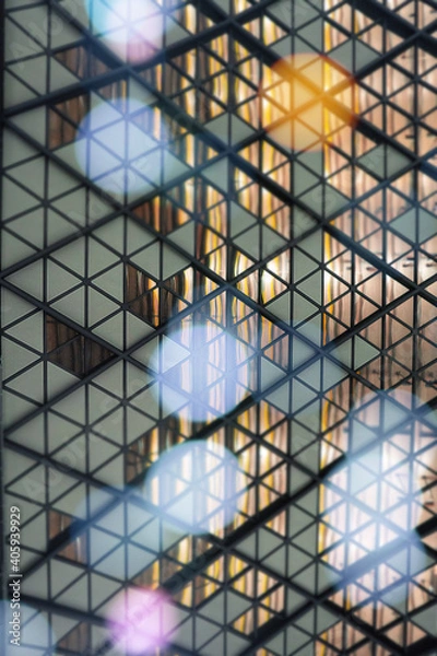 Fototapeta Modern glass wall from small triangles and bokeh lights on the forefront.