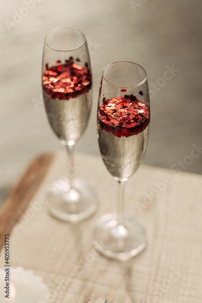 Fototapeta Happy Valentines day celebration concept. Close up of 2 two glasses with sparkling champagne and red heart shaped confetti. Love potion in glass