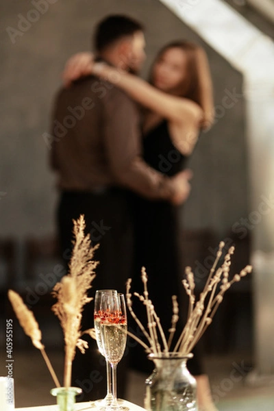 Fototapeta Well dressed stylish couple dancing at home. The concept of wedding, lovers day. Love and romance. A romantic date. Close up on glasses with sparkling champagne and red heart shaped confetti