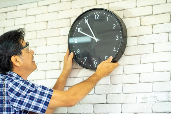 Obraz Asian technical engineer installing the clock on the wall in the office