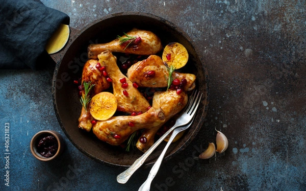 Obraz Fried chicken drumsticks with lemon and pomegranate seeds in a skillet