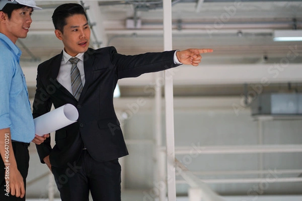 Obraz Asian engineer wearing hard hat talking with business man in formal suit in the factory