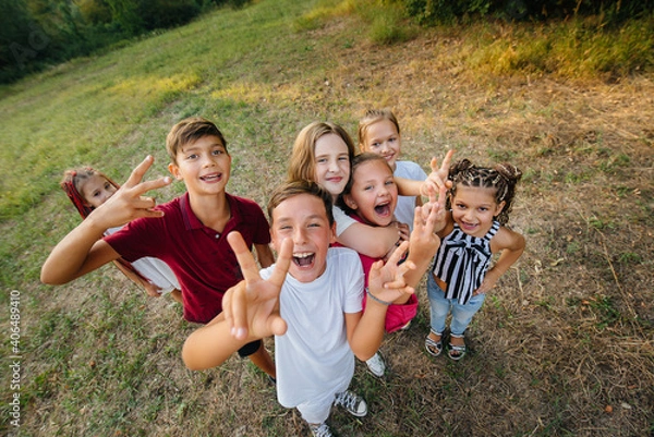 Fototapeta A large group of cheerful children sit on the grass in the Park and smile. Games in a children's camp