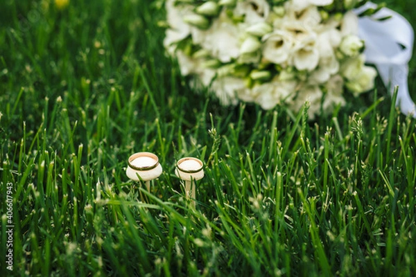 Obraz Beautiful wedding rings lie on wooden surface against background of bouquet of flowers. Declaration of love, spring. Wedding card, Valentine's Day greeting. Wedding rings. Wedding day details