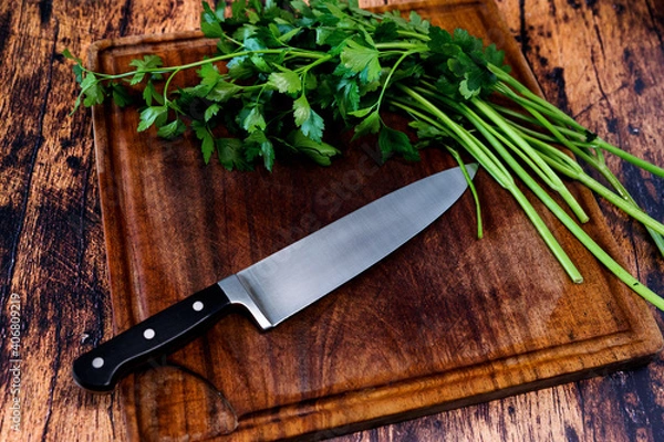 Fototapeta Worn wooden cutting board on an old worn wooden table with a knife on it and parsley