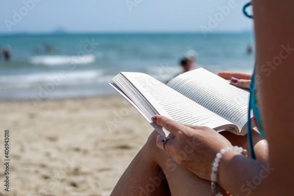 Fototapeta Woman reading a book on the beach, blurred background. Summer leisure on the beach