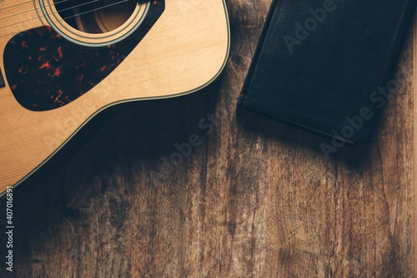 Fototapeta A guitar and a bible on a wooden background in a dimly lit environment. Soft light and worship