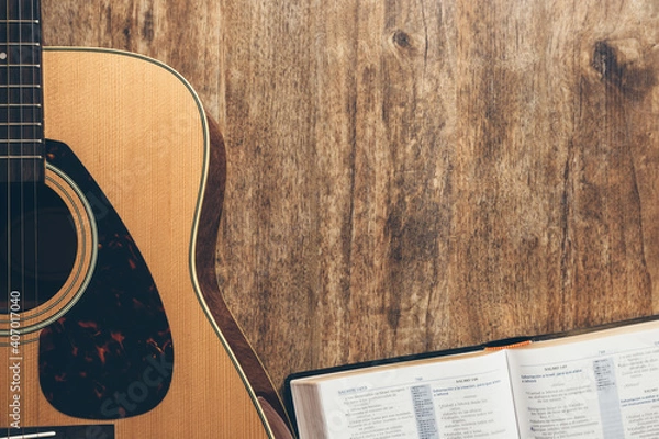 Fototapeta A guitar and a open bible on a wooden background in a dimly lit environment. Soft light and worship