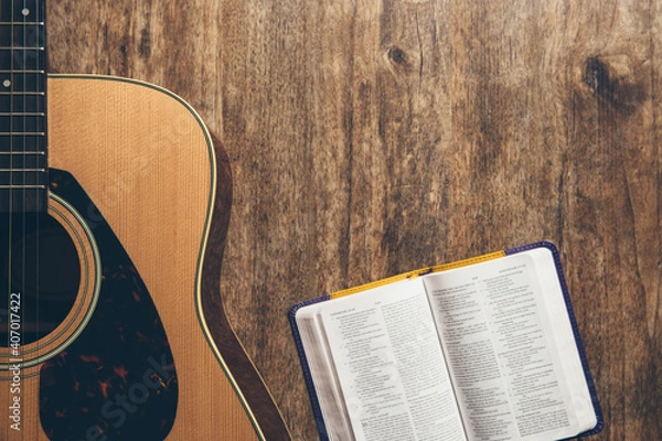 Fototapeta A guitar and a open bible on a wooden background in a dimly lit environment. Soft light and worship
