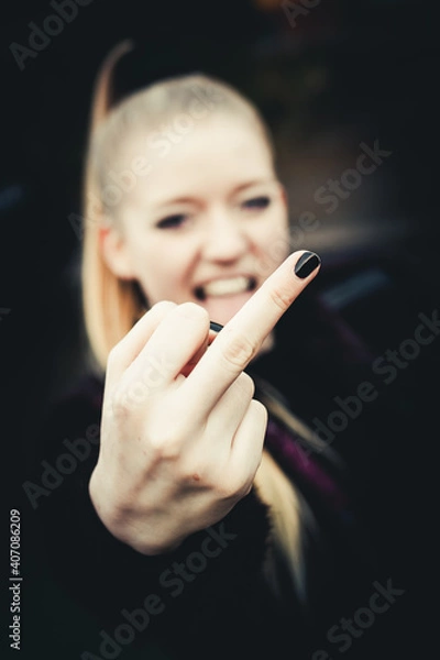 Fototapeta Pretty blond girl on dark background, flipping the bird at the camera