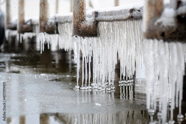Fototapeta long icicles hanging from an icy pier with balls at the end near the water