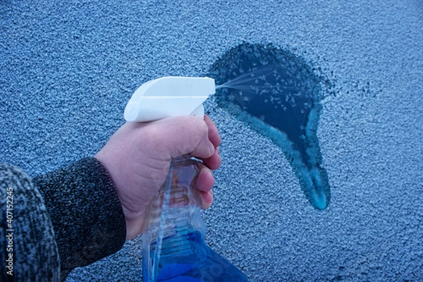 Fototapeta Remove ice from automobile windowshield. Hand with liquid spray for car window defrost in winter season. 