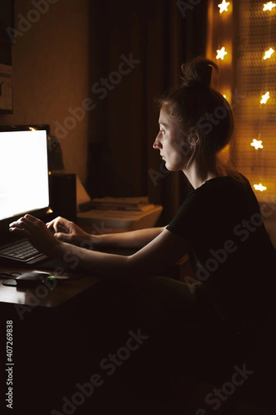 Fototapeta Young woman working late at night at the computer in home interior. Top view of the girl typing. Remote work, night waking, working overtime, finding information.