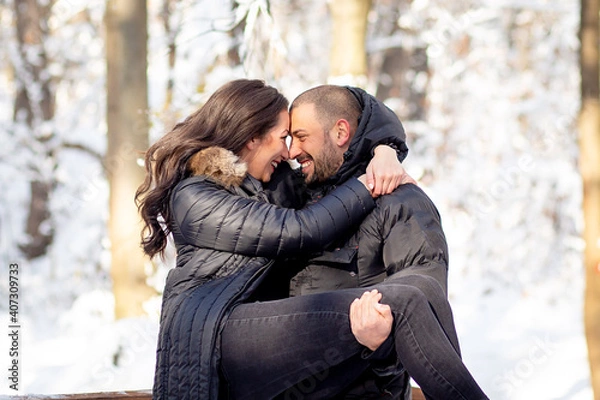 Fototapeta Man and woman in love hugging and kissing on a bridge. Snowy winter background.
