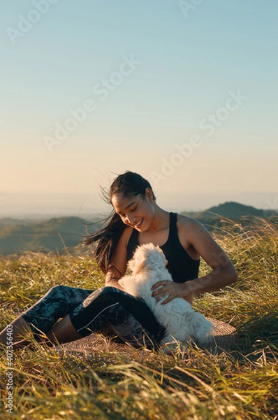 Obraz Happy young woman sitting on the grass playing with her beautiful puppy dog