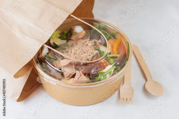 Fototapeta Fish diet salad with tuna, tomatoes, arugula on light background. Healthy vegetarian lunch. Concept eco restaurant delivery, environment protection. Take away food in brown paper craft plate. 