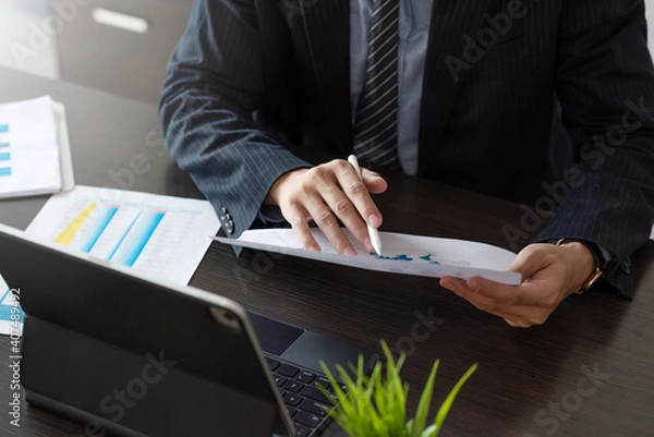 Fototapeta Businessman check information on document and a laptop on the table at the office.