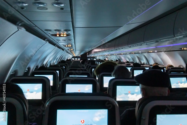 Fototapeta Plane cabin with passengers by night lit from screen (display) light