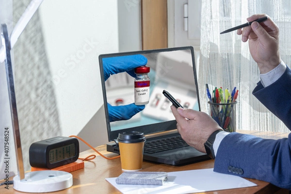 Fototapeta selective focus of a man in a blue suit medical director in confinement time looking at the mobile phone while being shown the Covid19 vaccine on the laptop