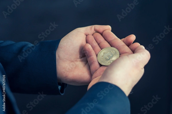 Fototapeta Virtual currency and blockchain concept. Businessman in a blue jacket holding Bitcoin in his hands.