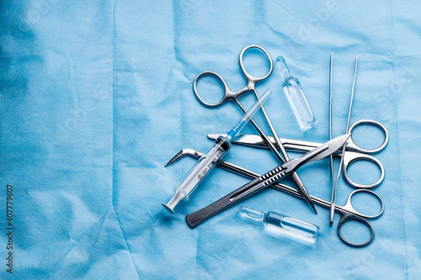 Fototapeta stack of surgical equipment at surgery desk. medical tools such scissors, scalpel, forceps, tweezers over blue background. surgery concept