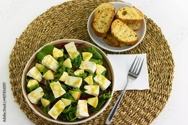 Fototapeta Mixed leaf salad with organic goat Camembert cheese and pears dressed with honey and mustard dressing on a plate. With toasted baguette slices on the side.