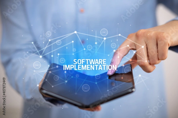 Fototapeta Businessman holding a foldable smartphone with SOFTWARE IMPLEMENTATION inscription, new technology concept