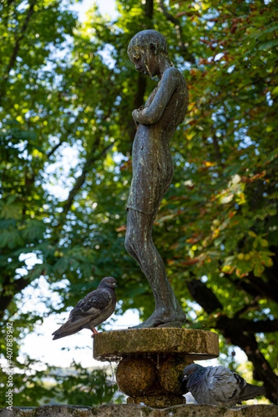 Fototapeta Bronze statue of a girl in the middle of a city garden. Fountain with pigeons taking a bath on a hot day. Alameda gardens.