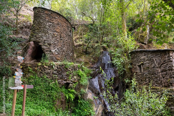 Fototapeta Watermill in the middle of a forest. Rustic building made of rock. Small waterfal. Hiking signs.