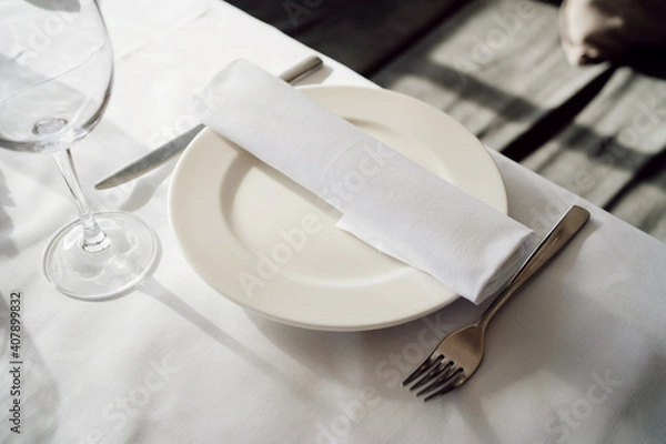 Fototapeta serving the table. white empty plate with napkin, knife and fork. festive banquet. service in a restaurant or cafe.