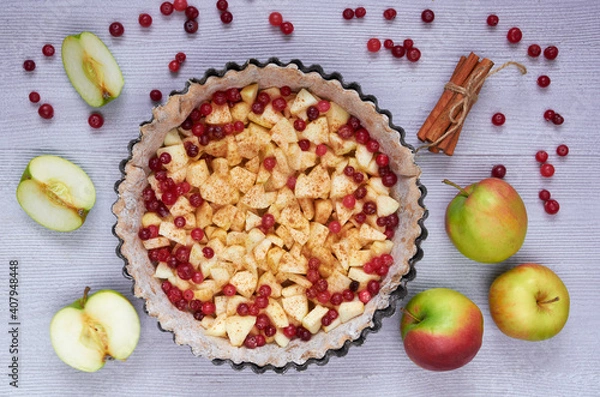 Fototapeta Apple tart in the
baking dish decorated with fresh apples, cranberry, spices, cinnamon sticks on the gray kitchen background. Autumn pie with raw ingredients. Top view