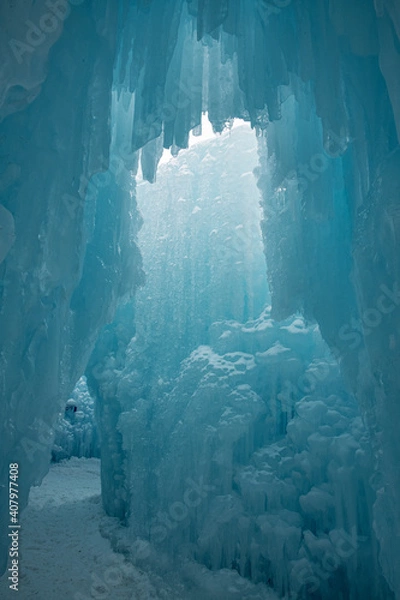 Fototapeta A walkway through ice. Blue and white icicles are hanging from above and the pathway is covered in snow.