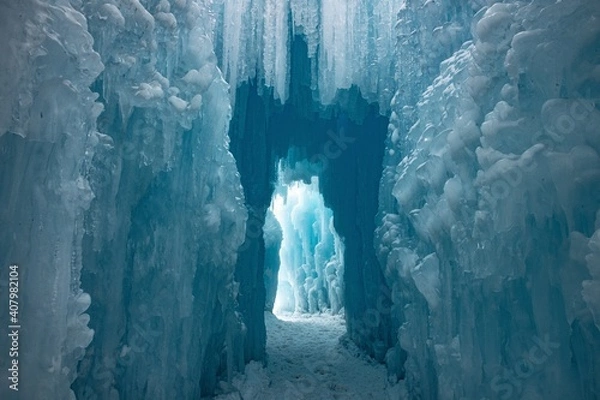 Fototapeta A walkway through ice. Blue and white icicles are hanging from above and the pathway is covered in snow.