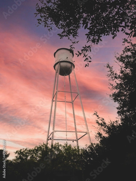 Obraz isolated Water tower against colorful sky with trees in foreground