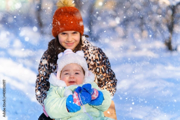 Fototapeta children sitting on sledge in the winter forest and playing, bright sunlight and shadows on the snow, beautiful nature