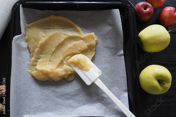 Fototapeta Top view of making roll-up pastila,homemade fruit leather . Fruit puree on a black baking sheet with a white spatula on a wooden table. The concept of making natural sweets from apples and bananas
